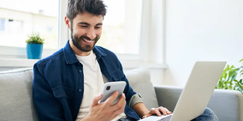 Un homme souriant utilisant son téléphone et son ordinateur portables