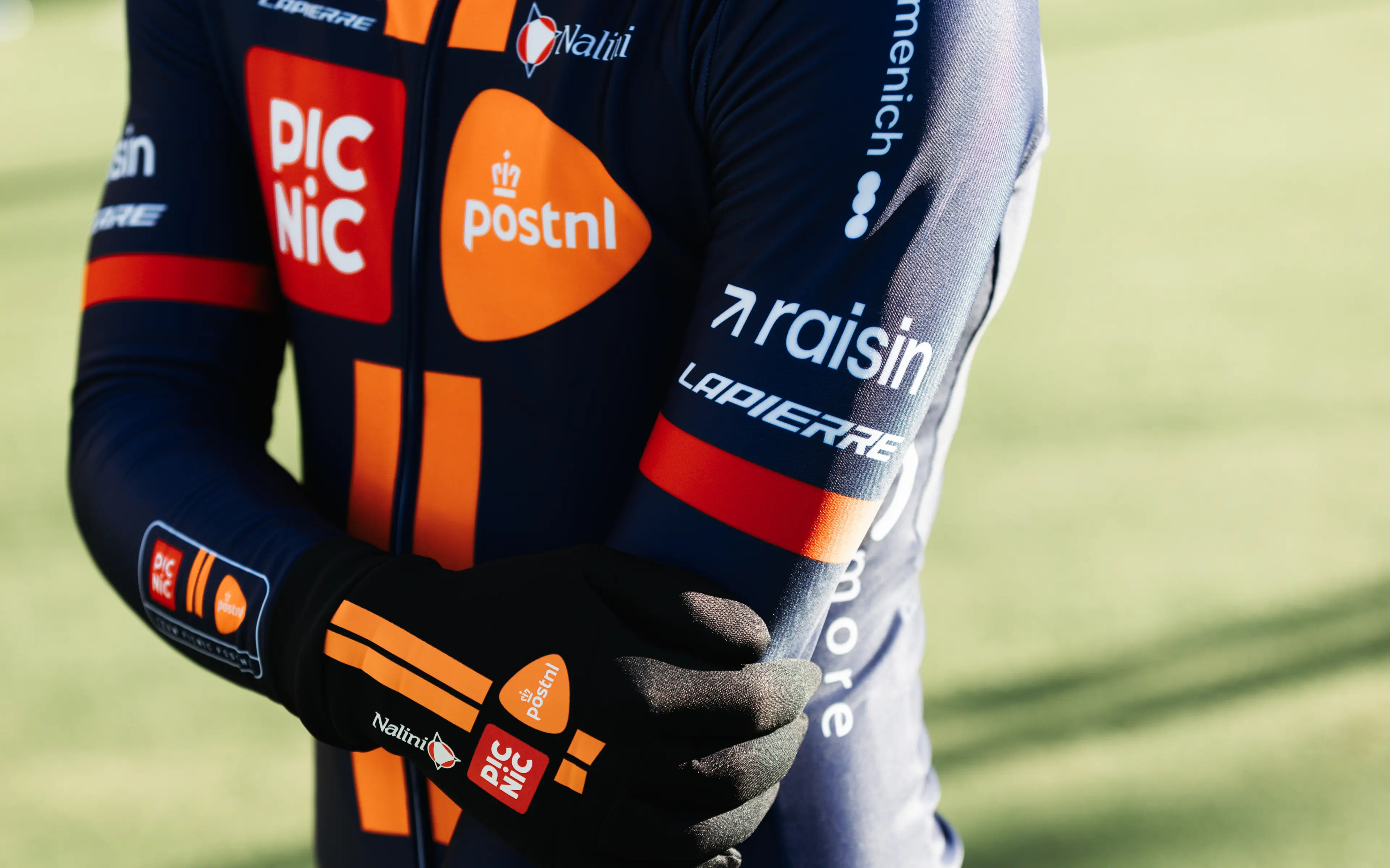 Raisin_Picnic_PostNL2 Close-up of a cyclist’s gloved hands and arm, wearing a Picnic PostNL team jersey with Raisin and Lapierre logos.