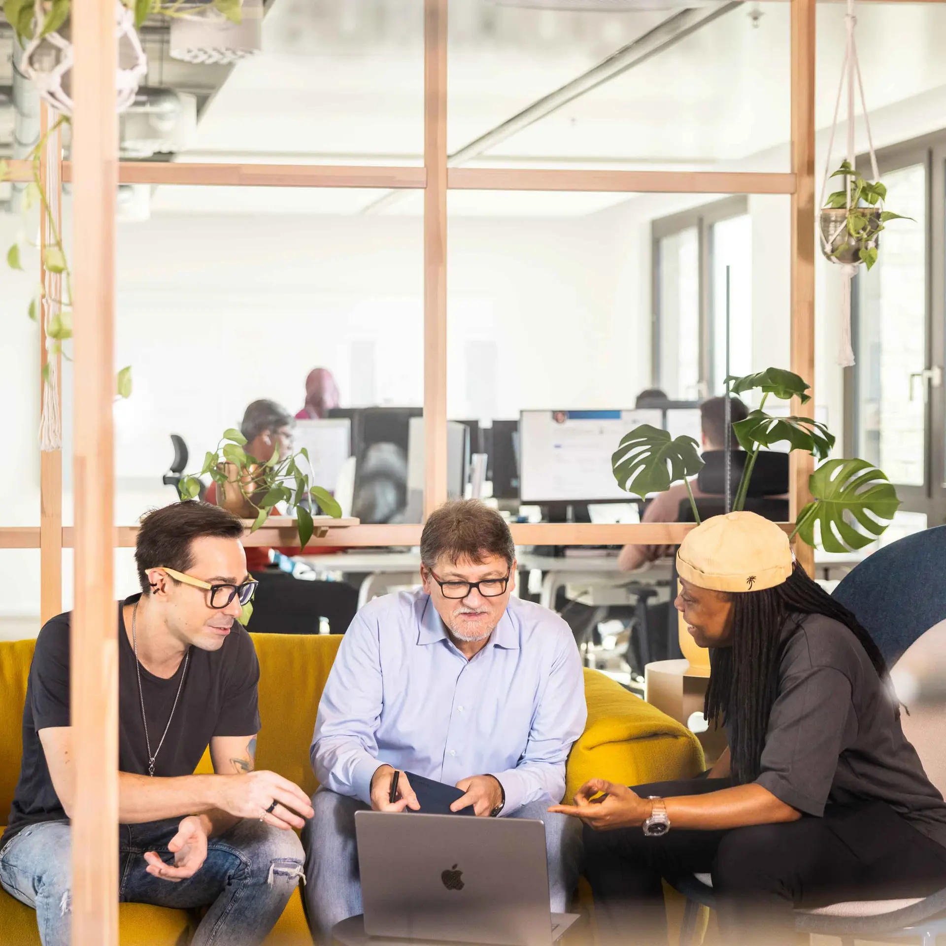 Three colleagues are sitting on a yellow sofa while looking at a notebook and discussing