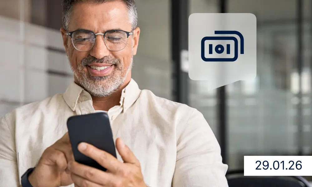 Raisin DE SEPA Instant Payments Ein Mann mittleren Alters steht in einem modernen Büro und schaut lächelnd auf sein Smartphone. Neben ihm ist ein Symbol für eine Sofortüberweisung zu sehen, unten rechts steht das Datum 29.01.26.